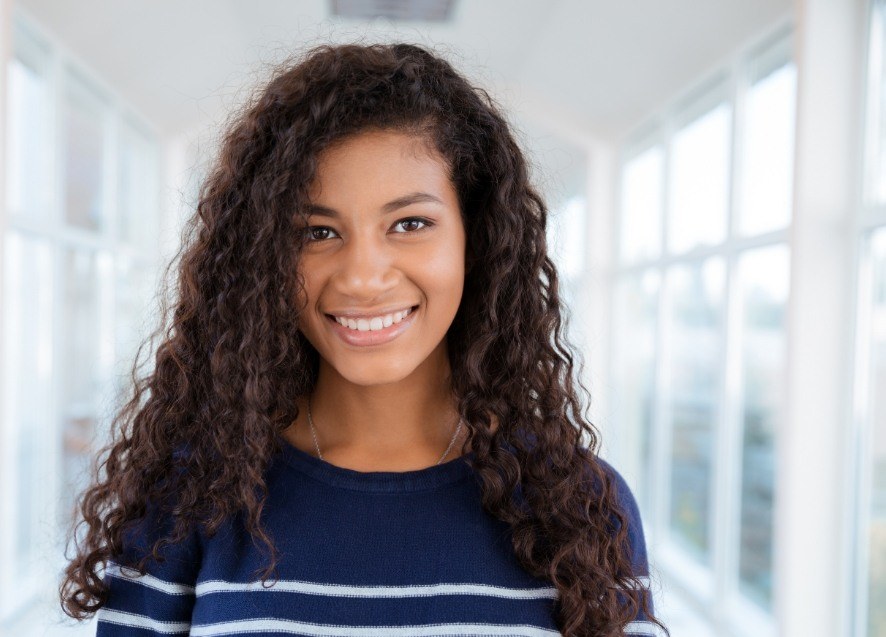 Teenage girl in dark blue sweater smiling after seeing dentist for teens in Murphy