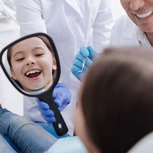 Child smiling at reflection in dental mirror at home