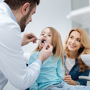 Dentist examining child's teeth with smiling mother