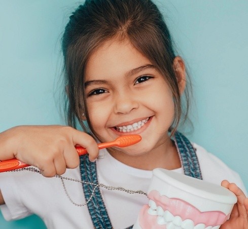 Smiling girl holding a toothbrush and a model of the teeth