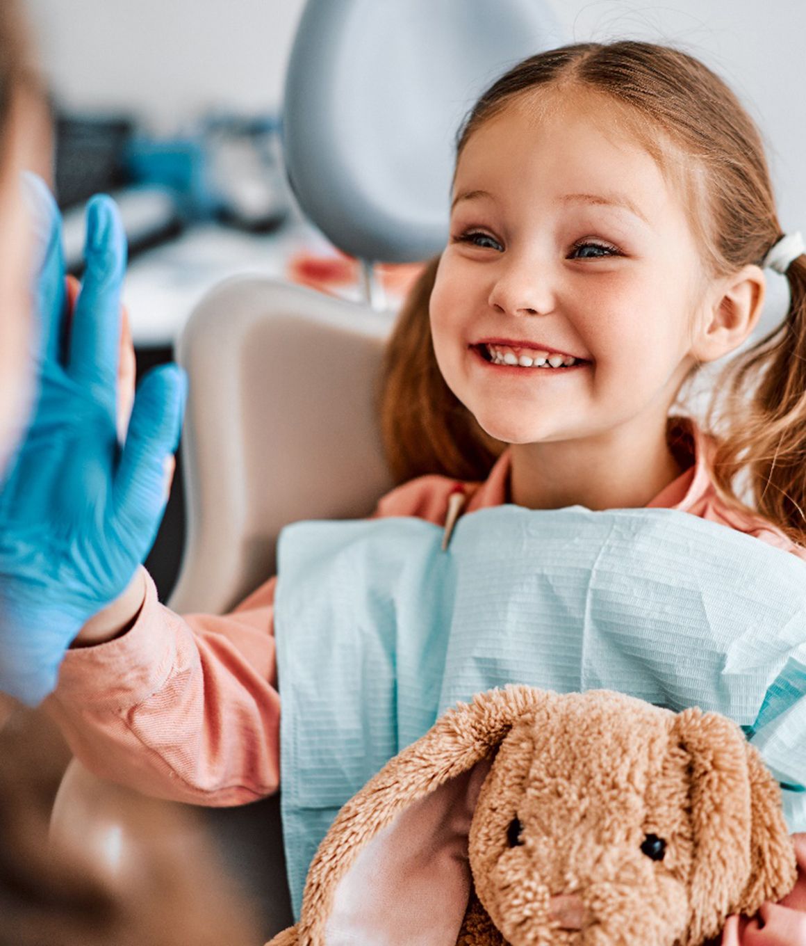 Child giving dentist high-five while holding stuffed animal