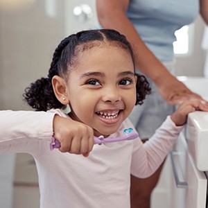 Child smiling while brushing their teeth at home