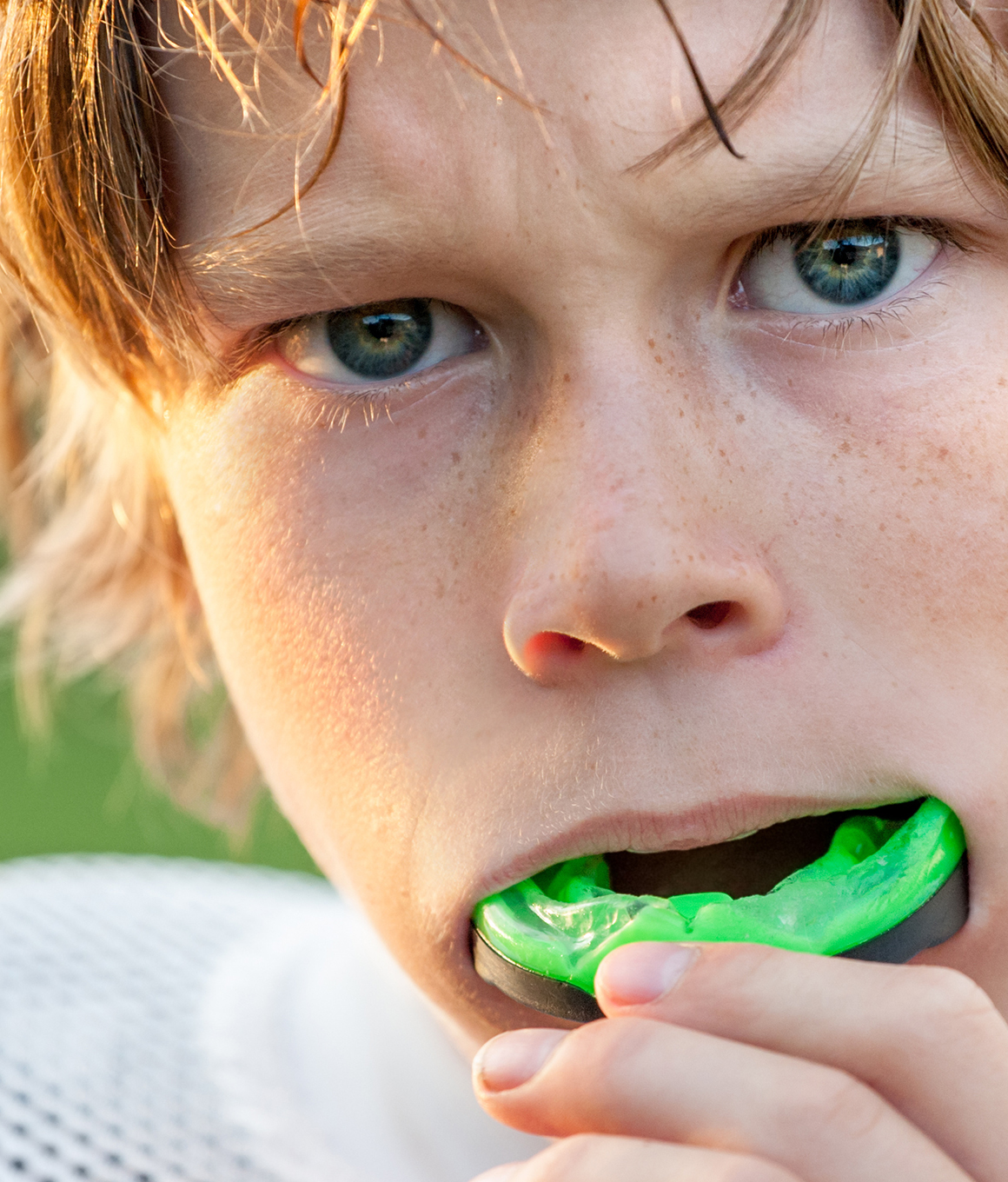 Boy placing green mouthguard over his teeth