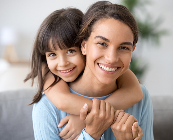 Smiling girl hugging her mother from behind