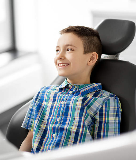 Boy in plaid shirt smiling in dental chair