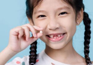 smiling little girl holding her extracted tooth